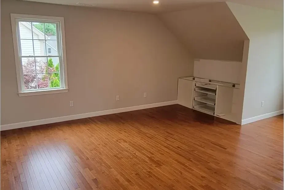 Empty sloped-ceiling room with hardwood floor, painted walls, recessed lights and open built-in shelving under the eave