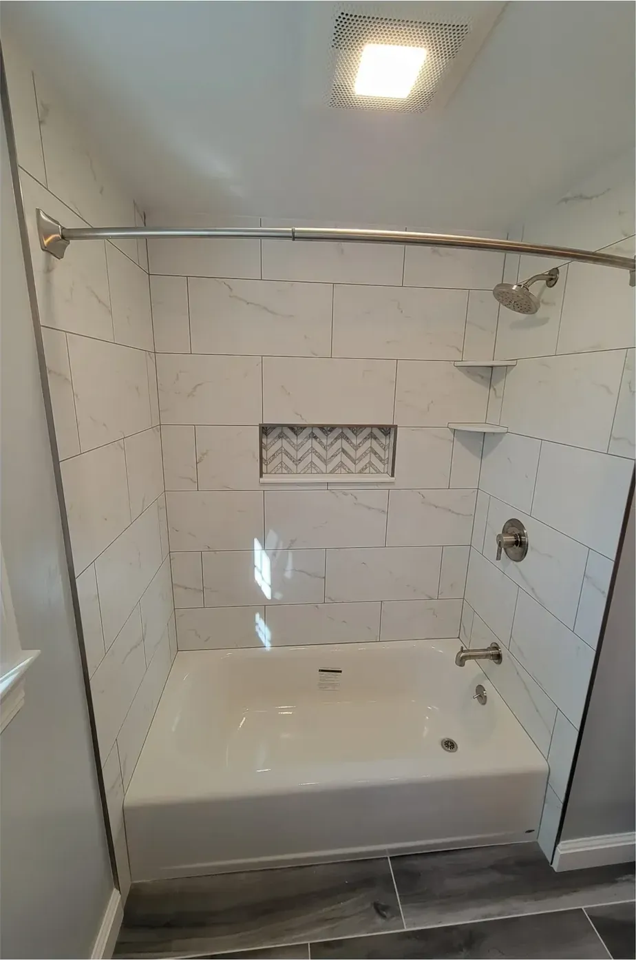 Tiled bathtub alcove with chevron mosaic niche, brushed nickel shower head, valve and curved curtain rod