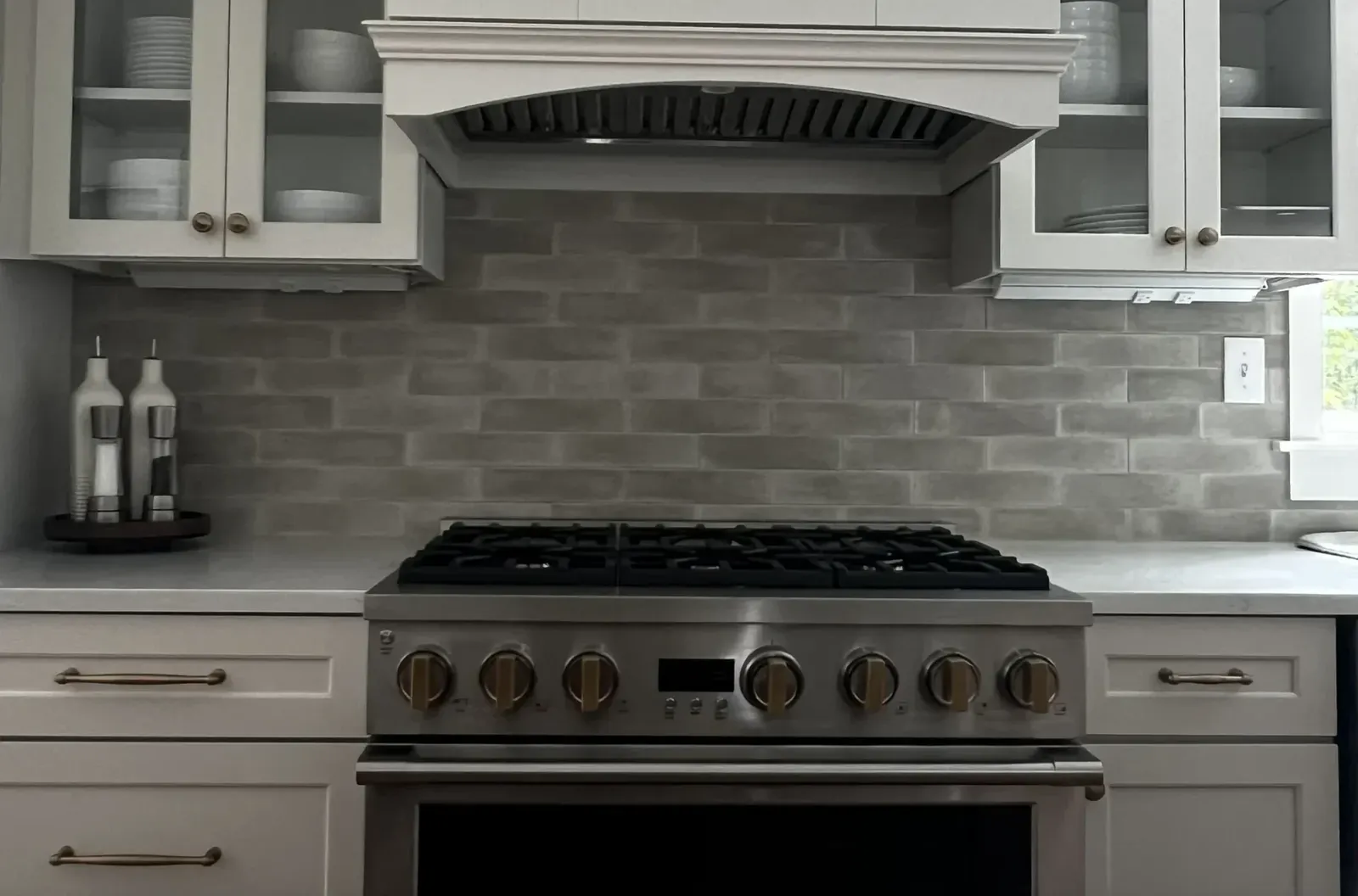 Stainless gas range under painted wood hood with grey tile backsplash and white cabinets